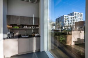 Kleine moderne pantry met koffieapparaat en spoelbak, met uitzicht op appartementencomplex aan de Fred. Roeskestraat.